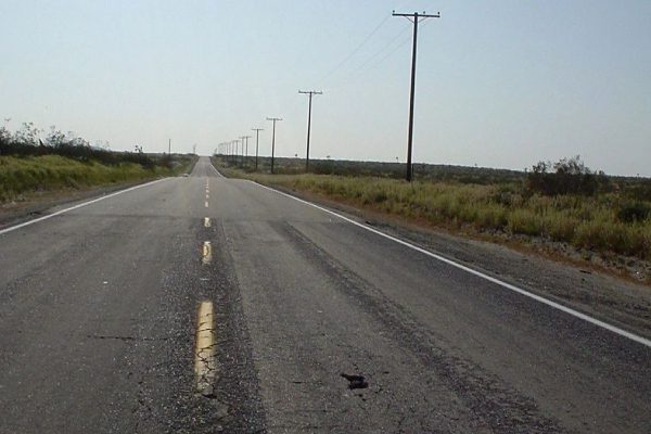 A road with no traffic on it and power lines in the background.
