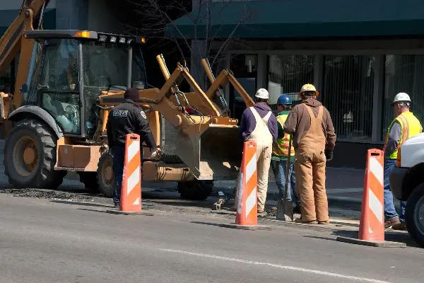 A group of construction workers standing on the side of a road.